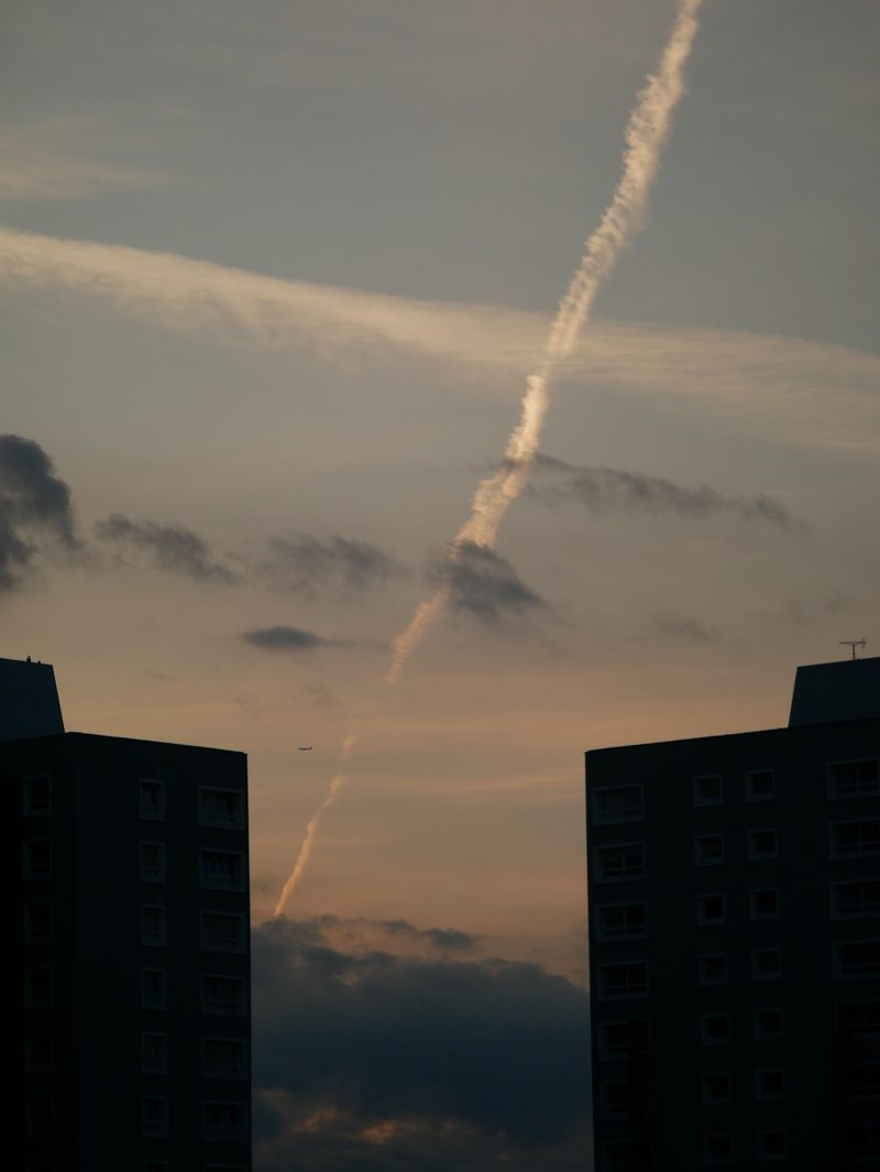 Contrails over rooftops at dusk